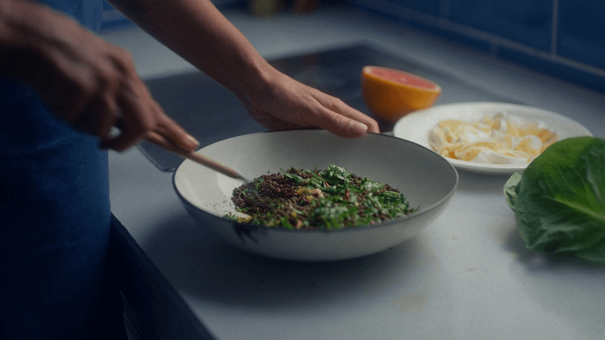 A pan of greens and herbs being finished by hand