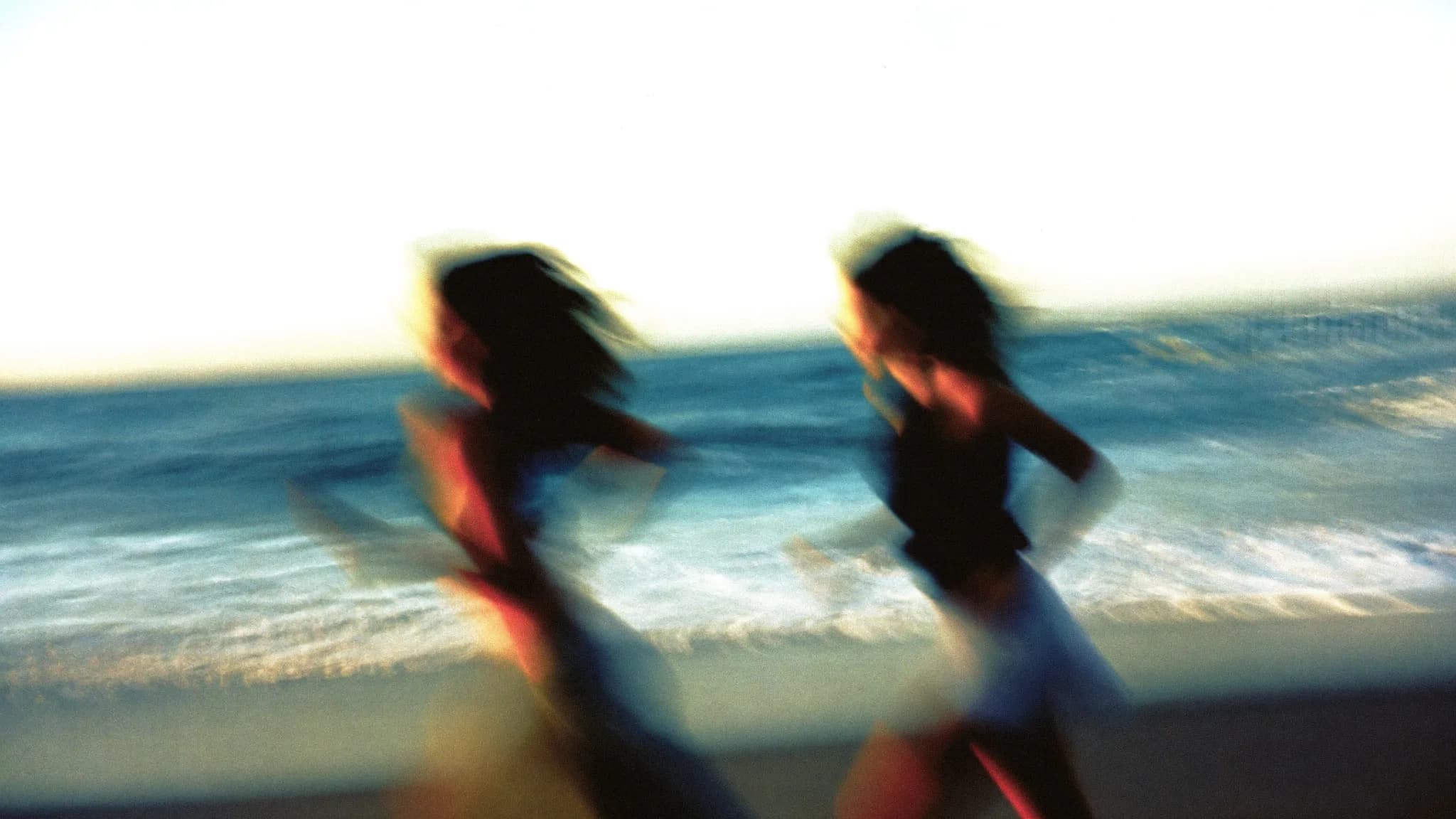 Two friends running along the shore at golden hour